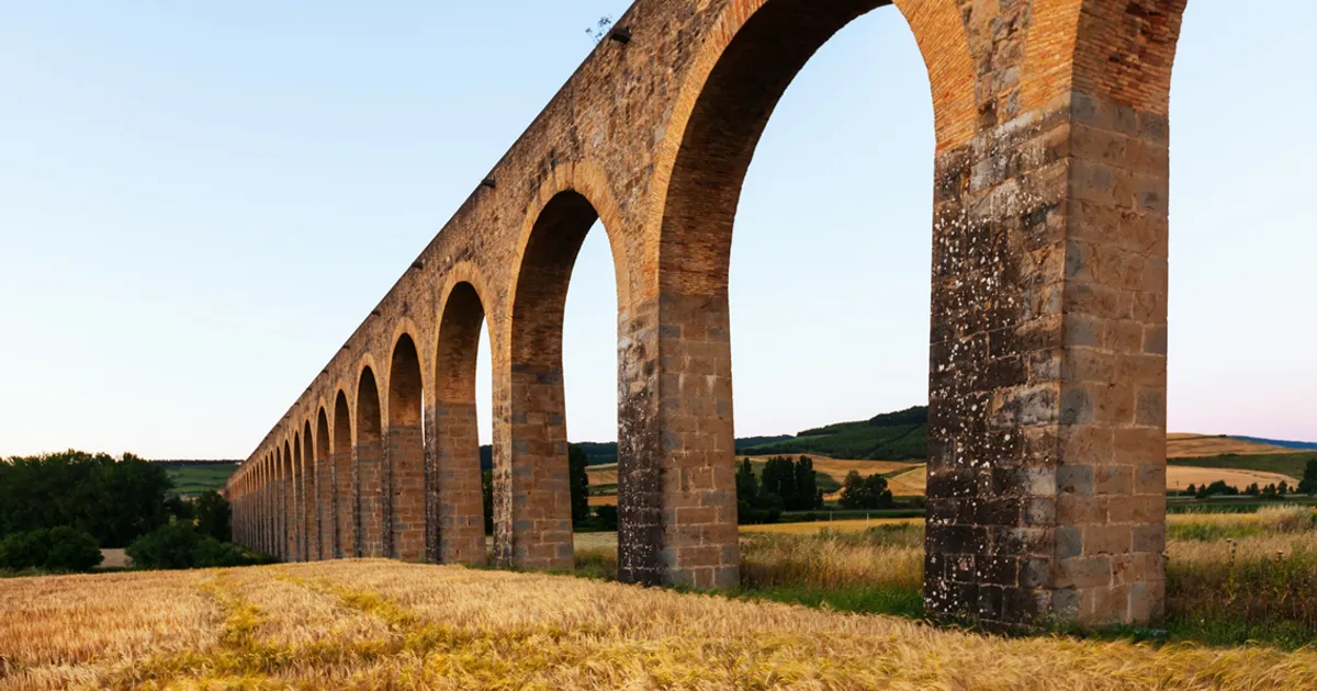 Acueducto romano de arcos de piedra sobre un campo de trigo al atardecer